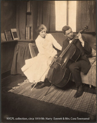 B&W sepia toned photo Cory & Harry e townsend at home Leonia NJ, 1919, sitting in living area, Harry holds a mucical instrument, a bass, appearing to play.
